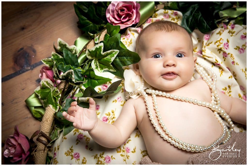 baby wearing pearls and surrounded by roses